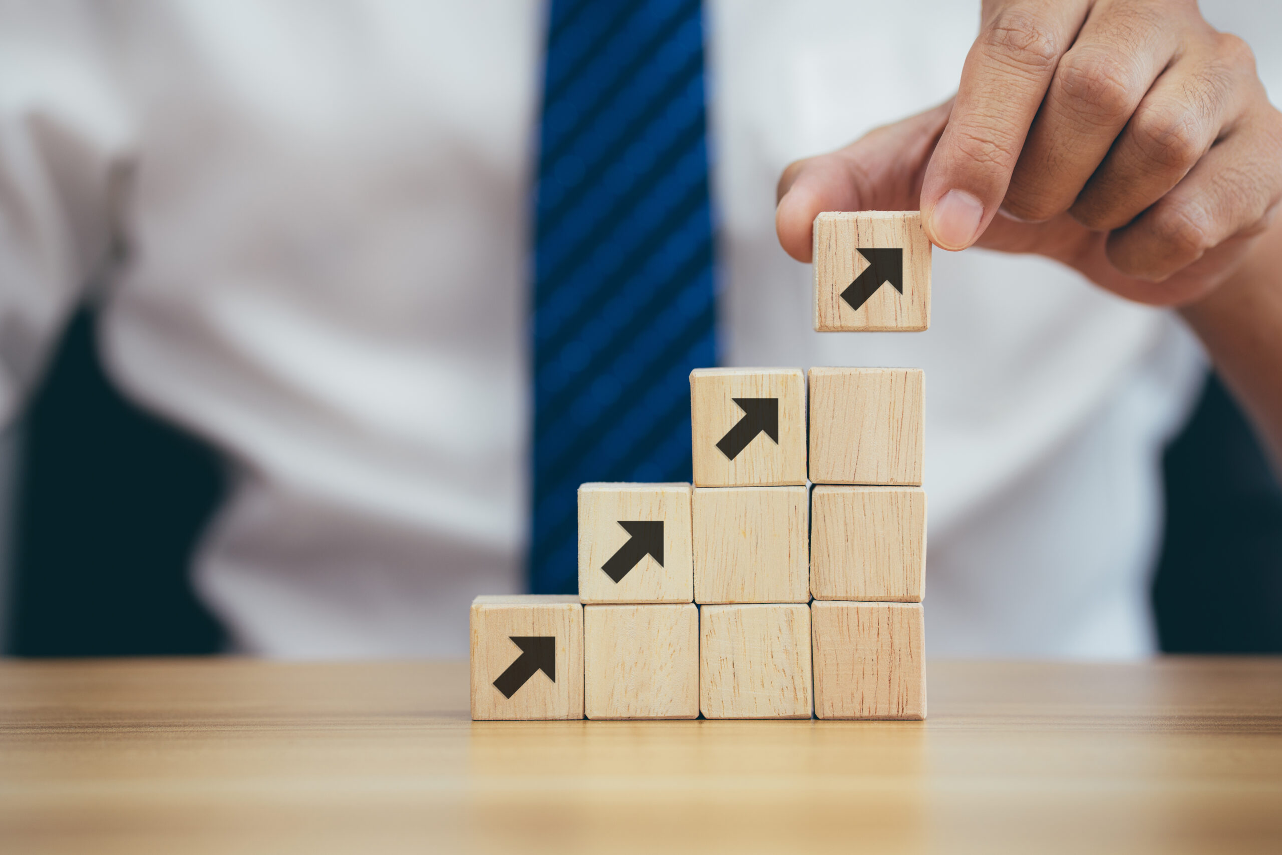 Closeup man hand arranging wood cube stacking as step stair to g Wooden blocks showing the building blocks of a successful business. Hand Me The Key provides small business coaching to help you thrive.