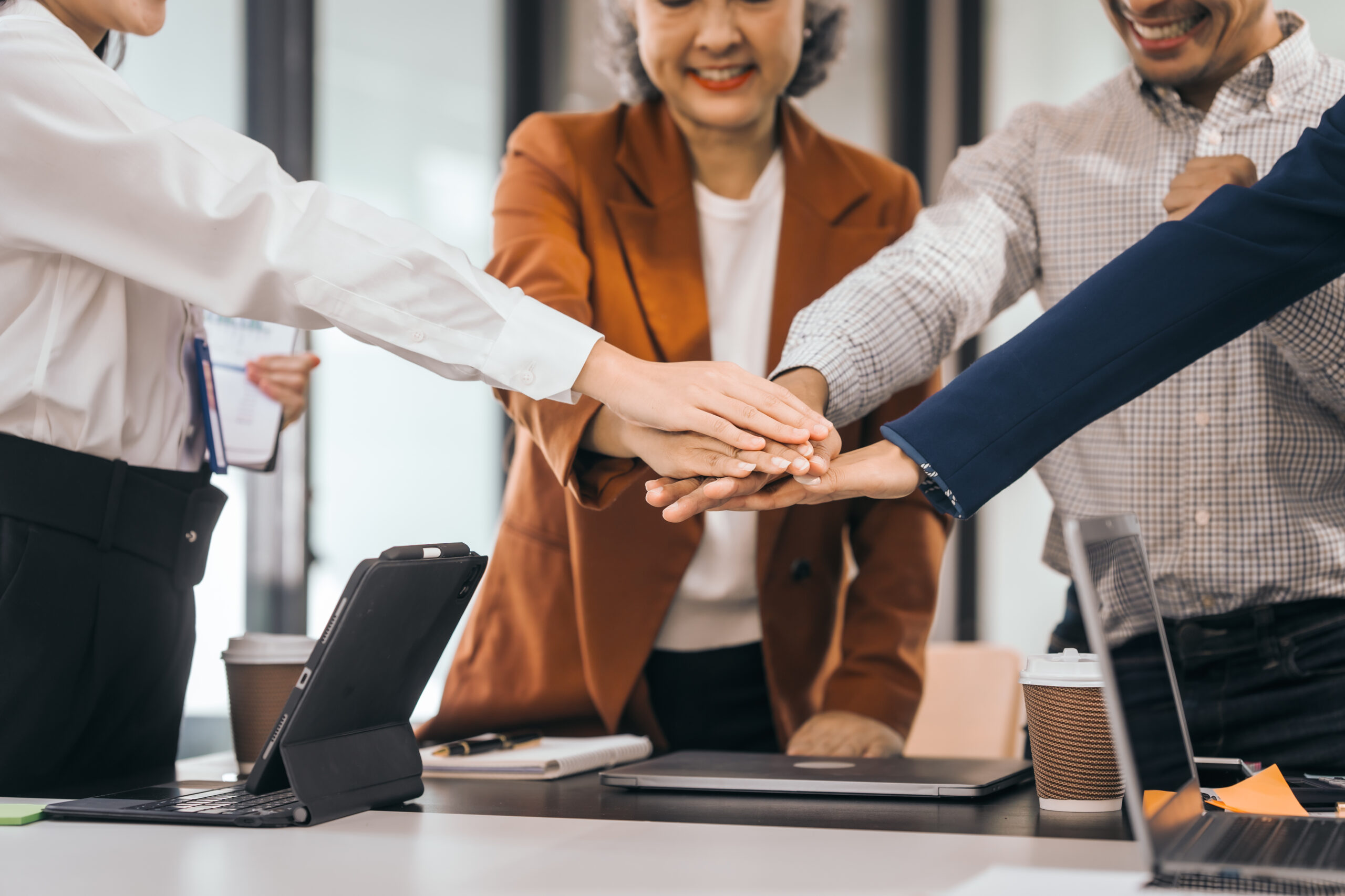 Four people in an office put their hands together as a team. They smile and wear work clothes. laptops, coffee, and papers on the table. They look cooperative. discuss opinions, presentation teamwork Wooden blocks showing the building blocks of a successful business. Hand Me The Key provides small business coaching to help you thrive.